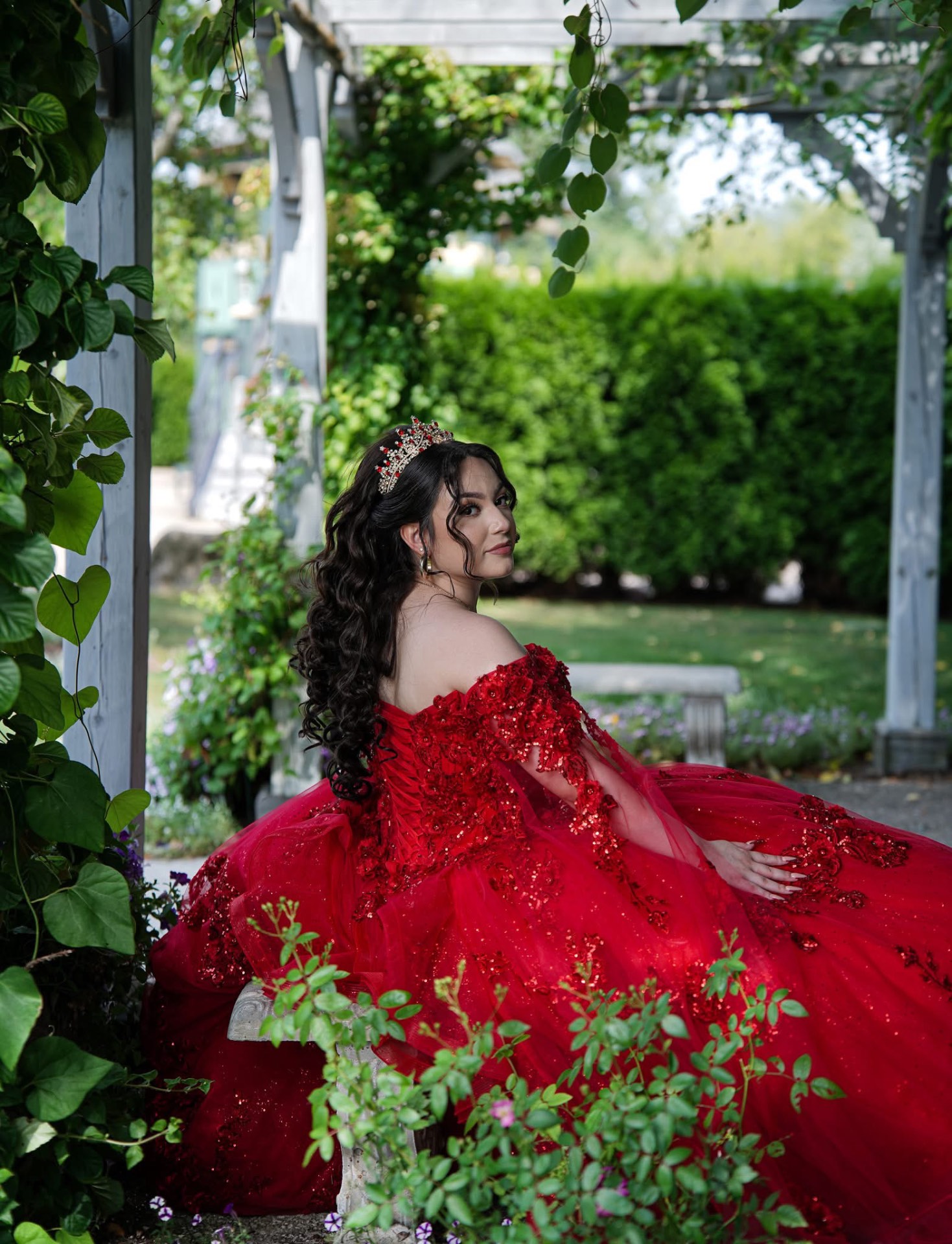 Portrait of a woman in a red gown seated in a garden pergola